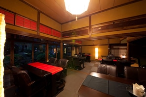 Interior de un restaurante con varias mesas y sillas, un ventanal con vistas a la vegetación y un techo de estilo japonés tradicional.