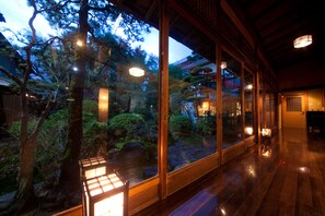 A traditional Japanese-style room with wooden flooring, large sliding glass doors, and a view of a garden with trees and a pond. - Ryokan Sennari (Beppu)