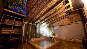 A traditional Japanese onsen with a stone bath, bamboo ceiling, and wooden shelves. - Ryokan Sennari (Beppu)