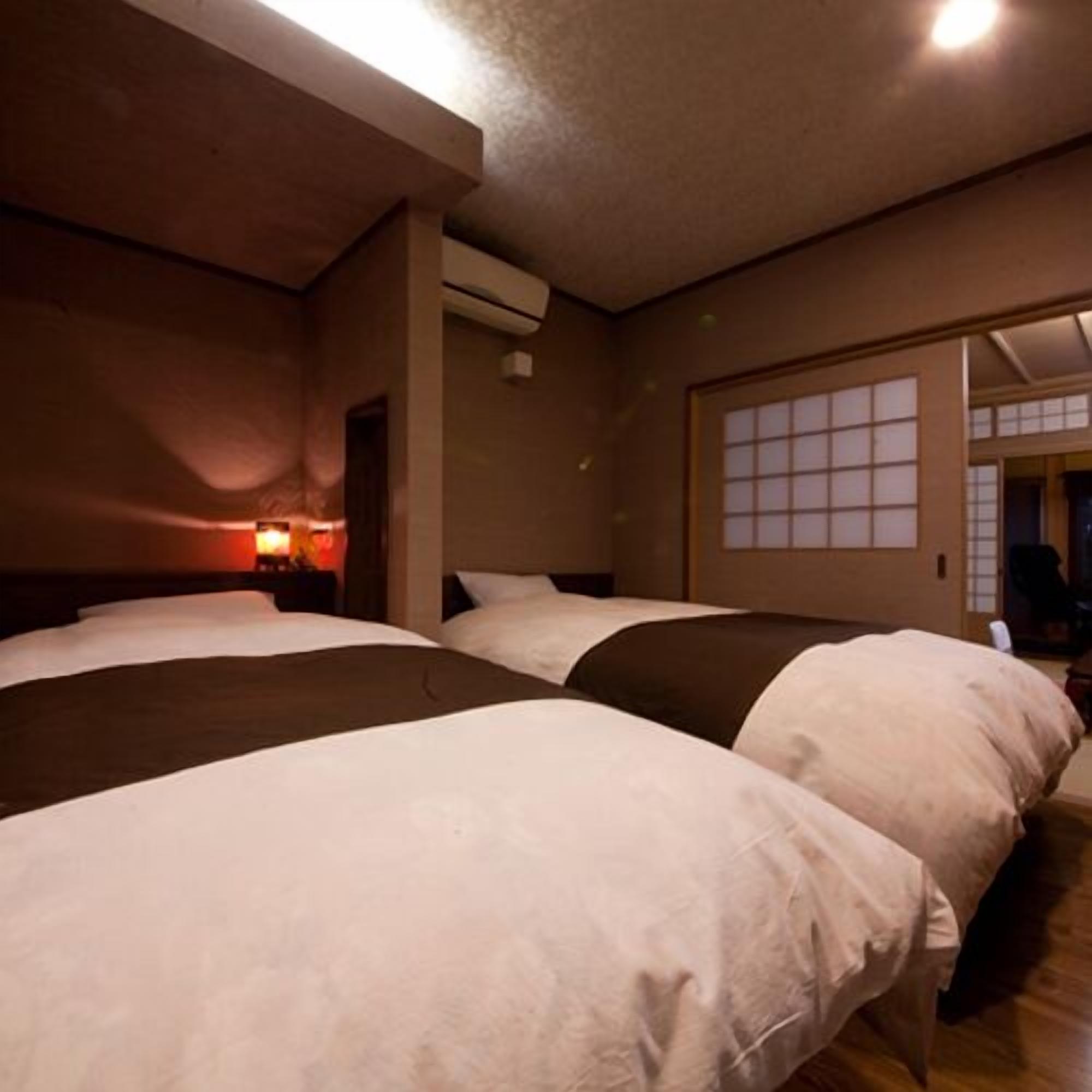 A hotel room with three beds, a nightstand with a lamp, a window with a view, and an air conditioning unit.