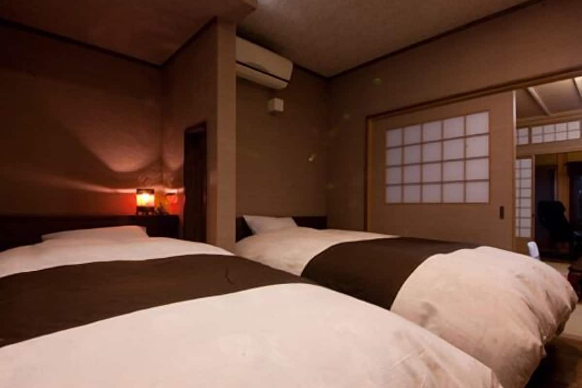A hotel room with three beds, a nightstand with a lamp, a window with a view, and an air conditioning unit.