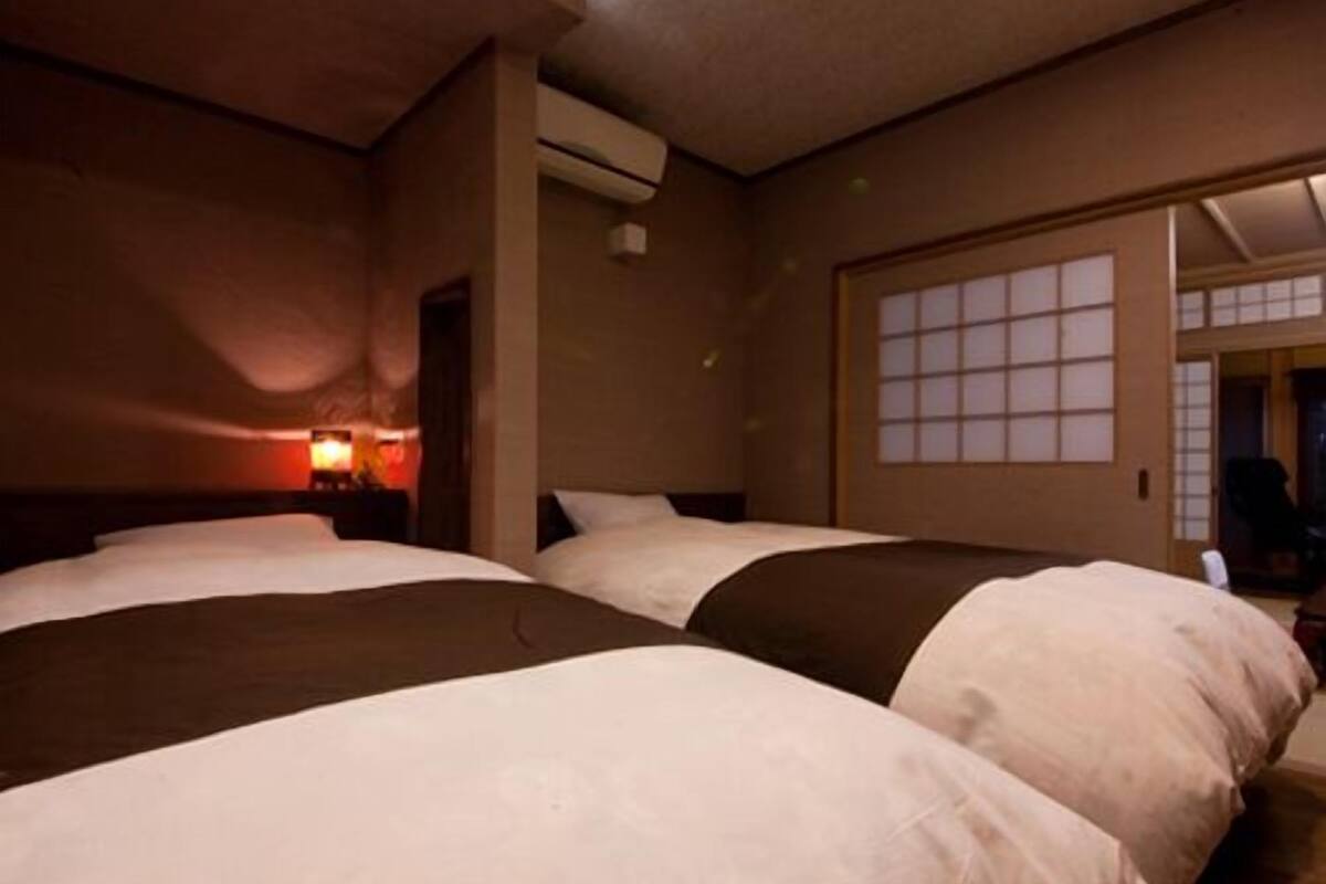 A hotel room with three beds, a nightstand with a lamp, a window with a view, and an air conditioning unit.