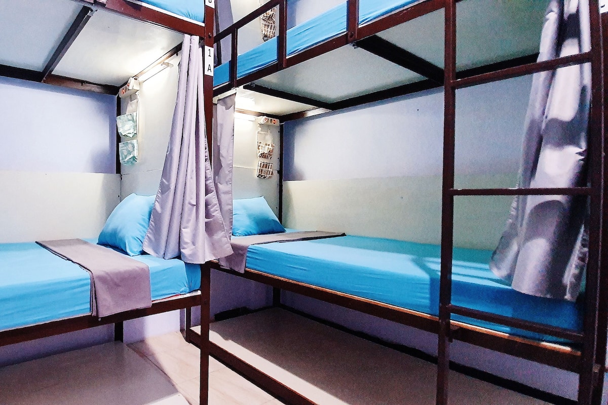 Une chambre avec un lit superposé, dotée de draps bleus et d’un rideau.