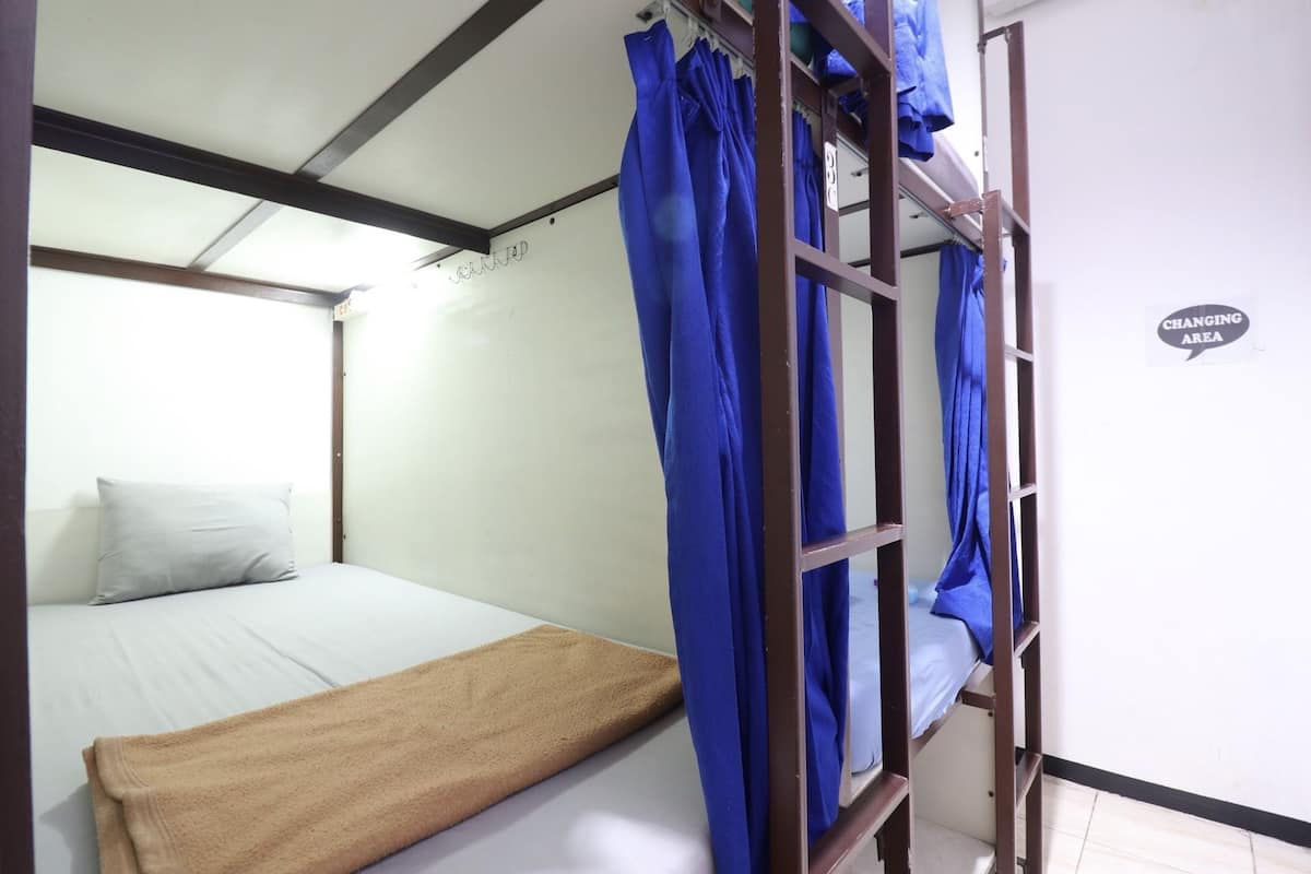 Une chambre avec un lit simple et un lit superposé. Un panneau sur le mur indique l’emplacement d’un espace pour se changer.