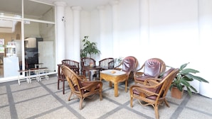 Una habitación con suelo a cuadros, columnas blancas, sillas de mimbre, una mesa redonda y una planta en maceta.