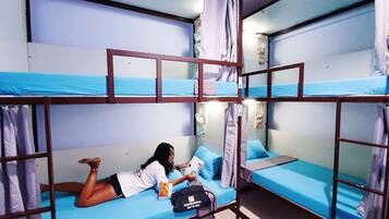 A bunk bed room with a person lying on the lower bunk, a backpack on the floor, and a suitcase on the bed.