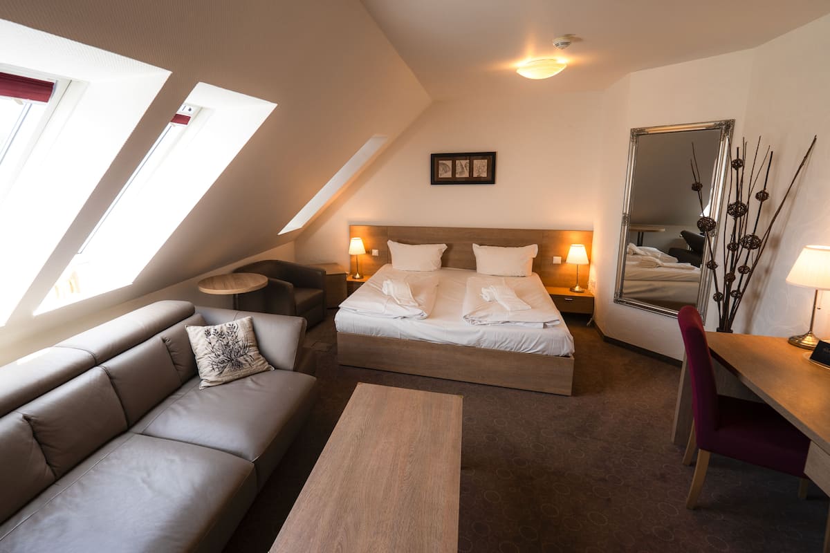 A modern hotel room with a bed, a sofa, a coffee table, a desk, and a large mirror.