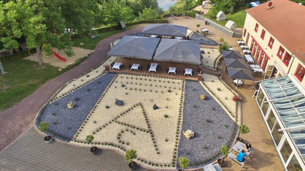 An outdoor seating area with tables and umbrellas, surrounded by a landscaped garden with gravel paths and potted plants. - Bernstein Acamed Resort (Nienburg)