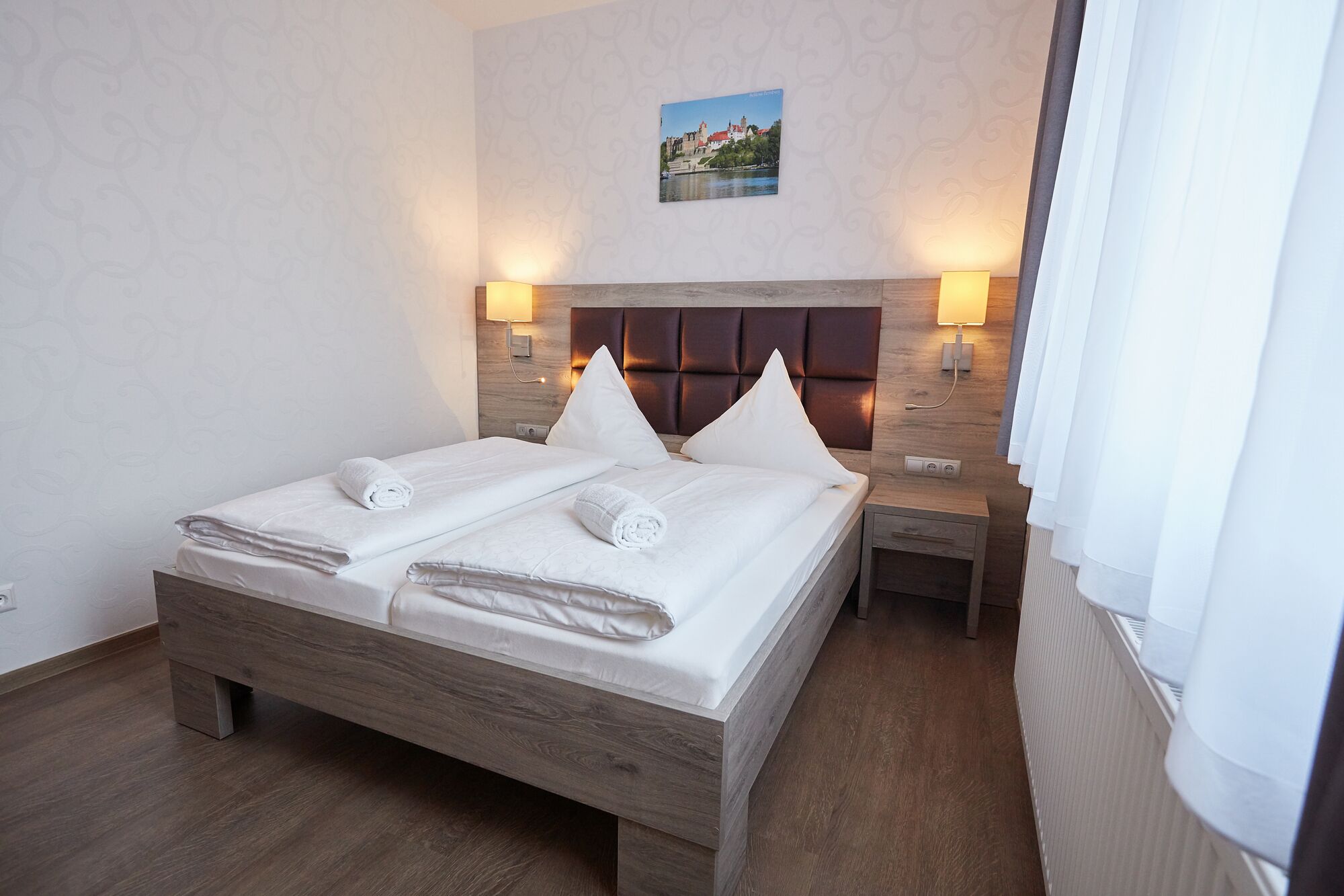 A hotel room with a double bed, two bedside tables, a headboard, and a wall-mounted picture.