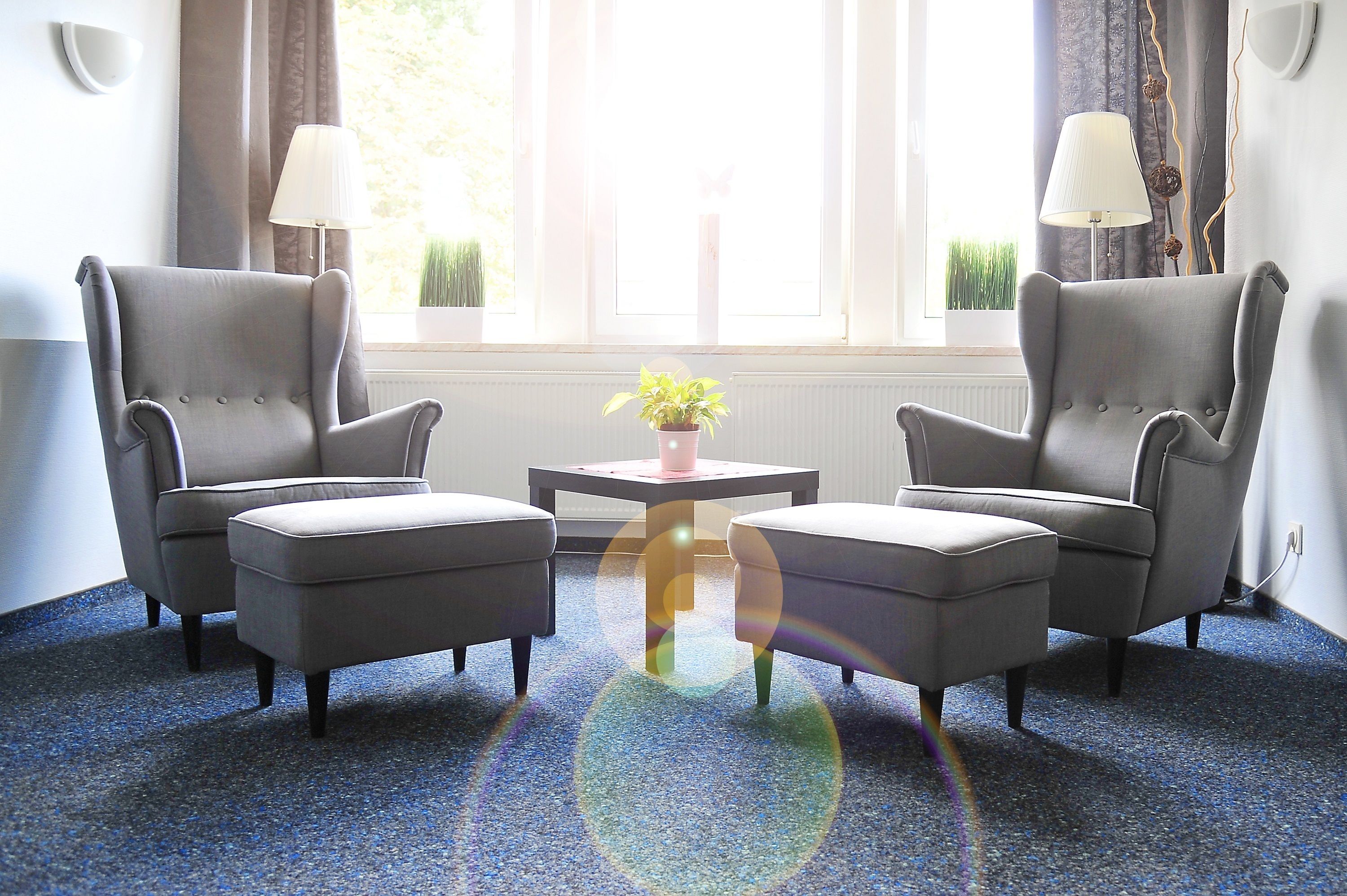 A room with two grey armchairs, a small table with a potted plant, and a window with curtains.