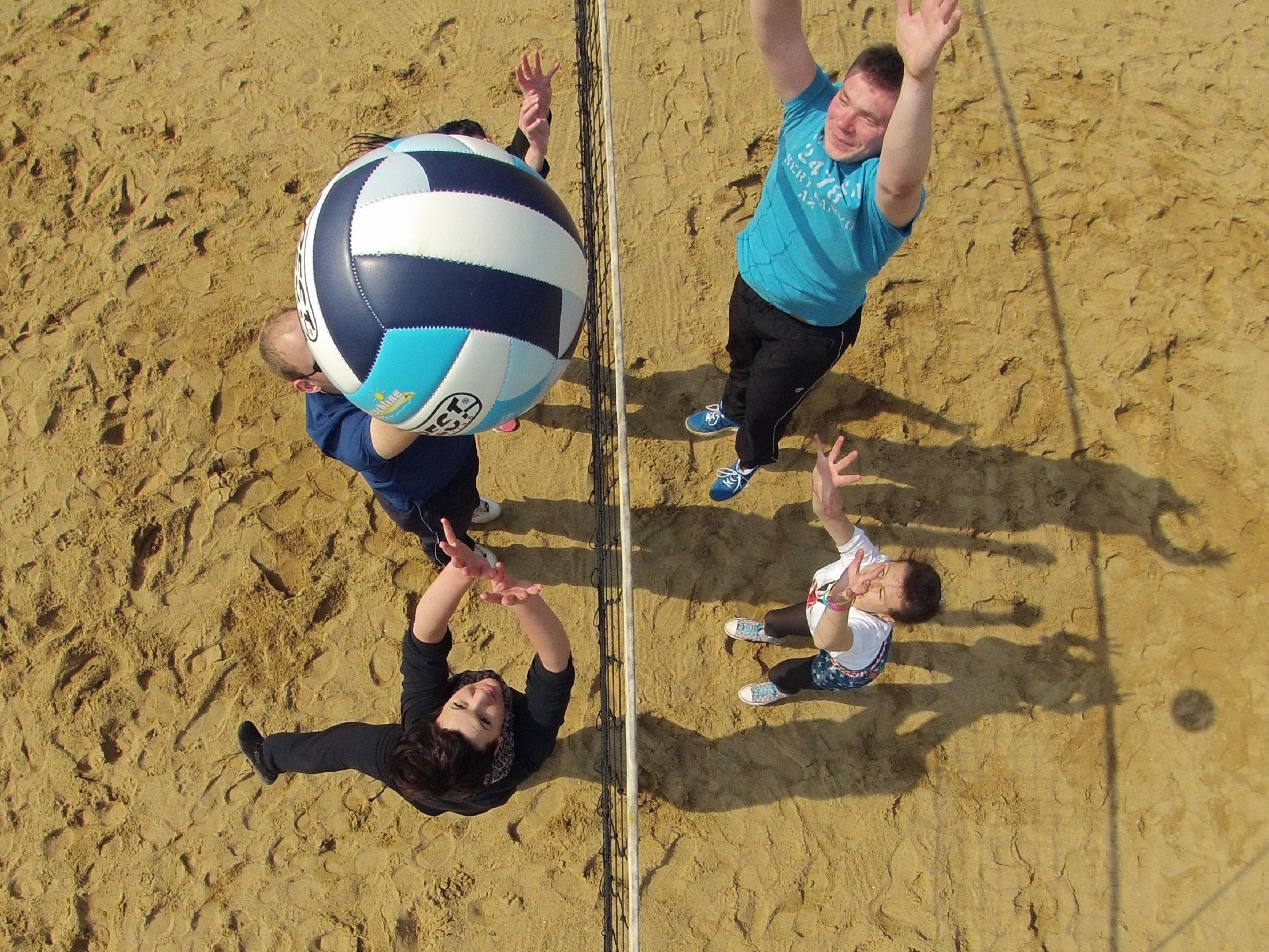 A volleyball game on a sandy beach with players and a volleyball net.