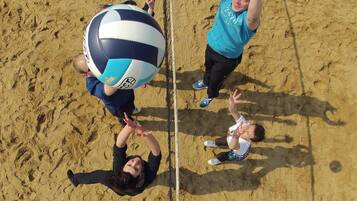 A volleyball game on a sandy beach with players and a volleyball net.