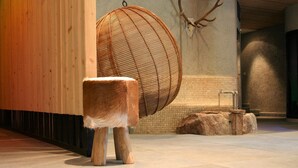 Un taburete de madera, una cesta tejida y una base de piedra en una habitación con paredes de azulejos y suelo de piedra.