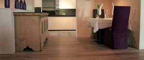 A narrow hallway with wooden flooring, a kitchen area with cabinets and a countertop, and a dining area with a table set for two. - MONTAFON Lodge Hotel und SPA (Gaschurn)