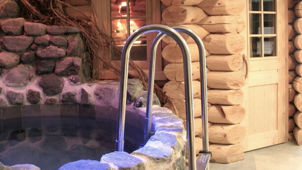 Un jacuzzi con escaleras metálicas, rodeado de muros de piedra y madera.
