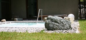 A swimming pool with a metal ladder, surrounded by rocks and pebbles, with a grassy area in the foreground. - MONTAFON Lodge Hotel und SPA (Gaschurn)