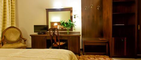 Une chambre d’hôtel comprenant un lit, un bureau avec un miroir, une chaise, une armoire et une petite table avec une plante.