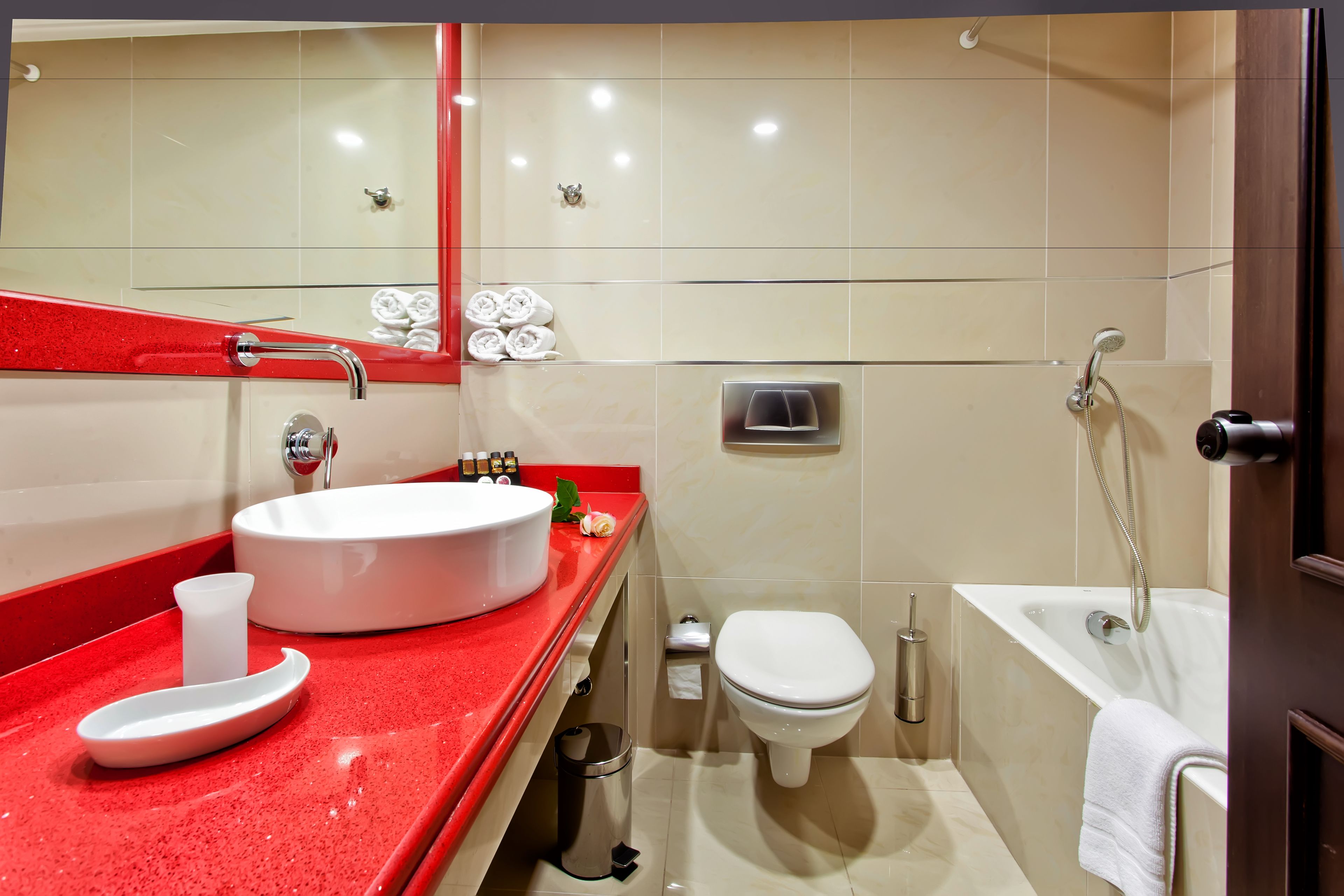 Une salle de bain moderne avec un plan de toilette rouge, un lavabo blanc, des toilettes et une baignoire.