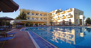 Un hotel con piscina, mobiliario exterior y un edificio de varios pisos con balcones.