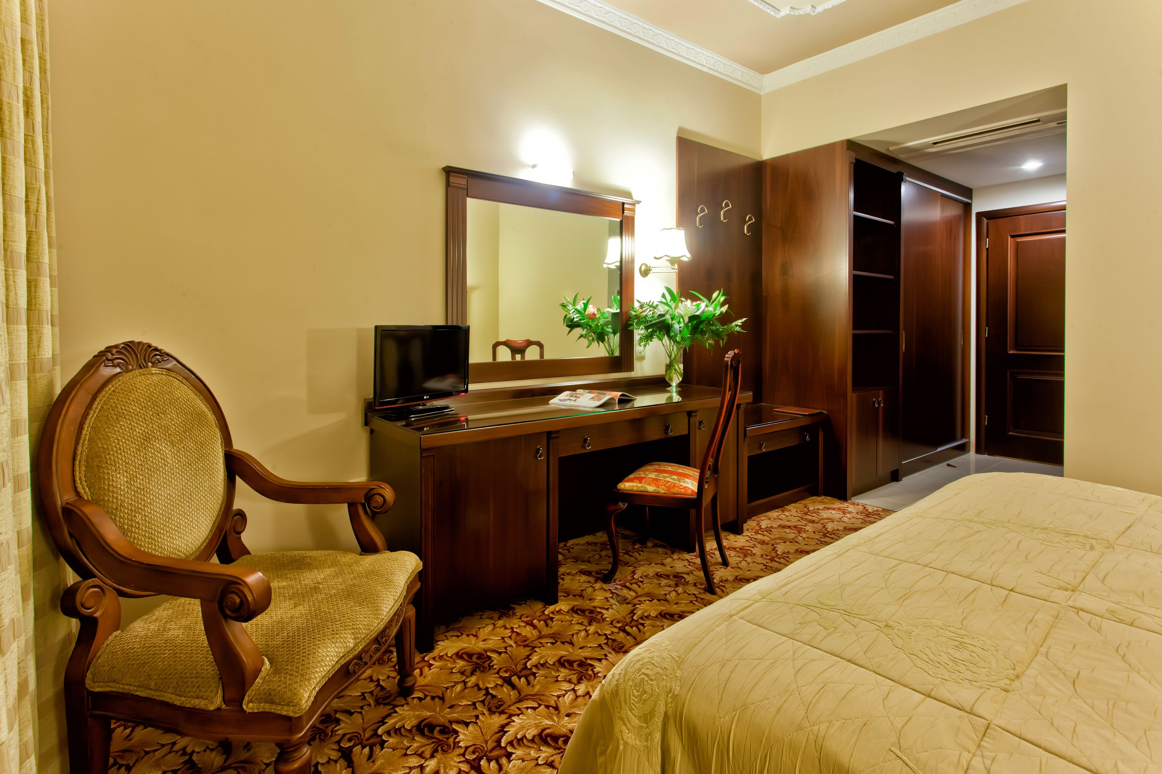 A hotel room with a bed, a desk with a chair, a dresser, and a large mirror.