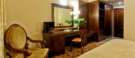 A hotel room with a bed, a desk with a chair, a dresser, and a large mirror.