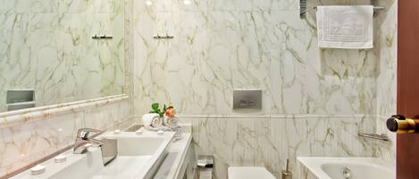 Un baño con pared de mármol, un lavabo, un inodoro y una bañera.