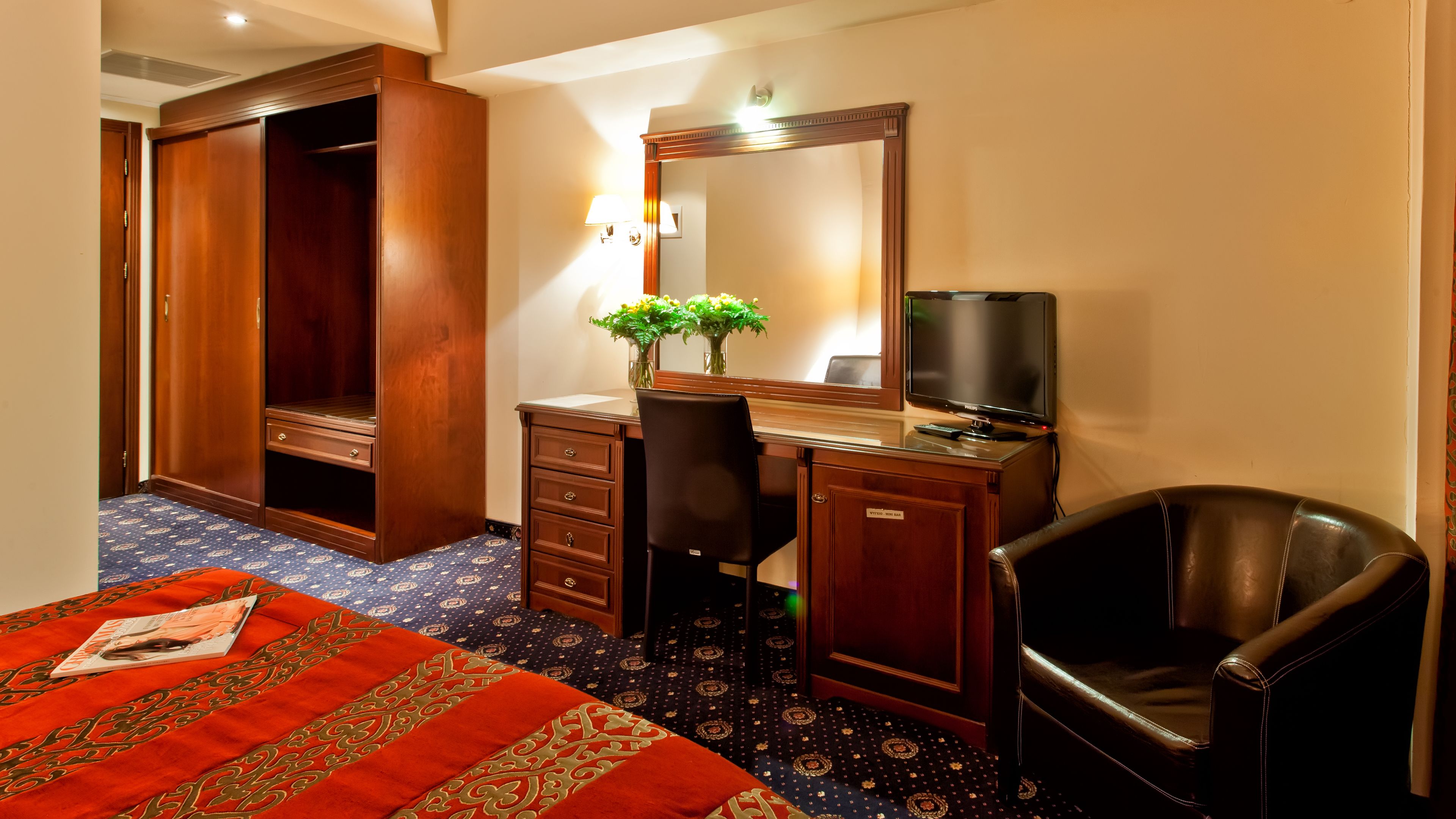 A hotel room with a bed, a desk, a chair, a television, and a wardrobe.