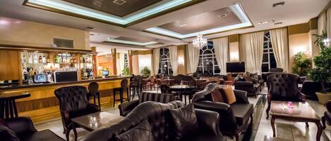 A spacious lounge area with leather sofas, a bar, and a chandelier.