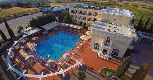 Vista aérea de un hotel con piscina, tumbonas y aparcamiento.