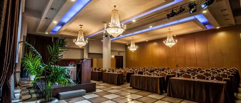 A conference room with a checkered floor, rows of tables, and chandeliers.