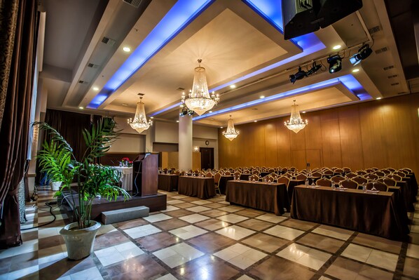 Un salón de conferencias con suelo a cuadros, mesas dispuestas en filas y candelabros.