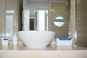 A bathroom with a large white bathtub, a blue shower seat, and a round mirror on the wall.