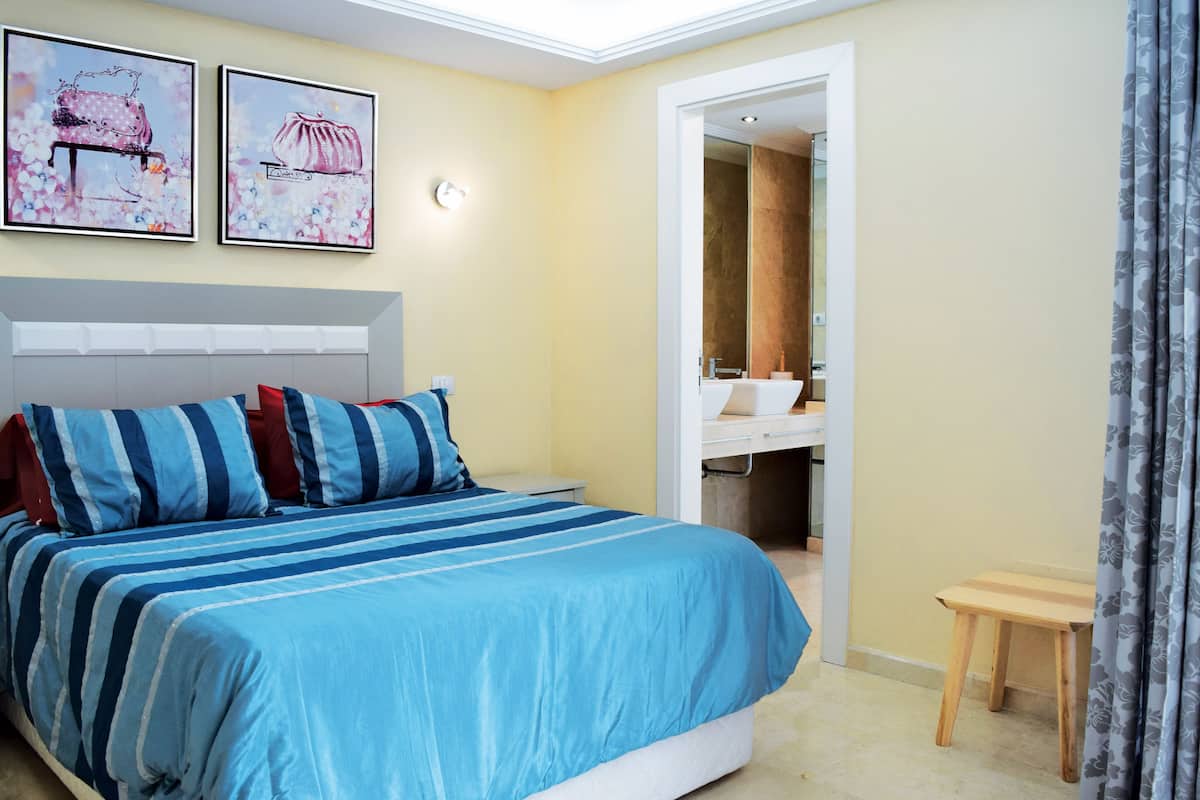 Un dormitorio con una cama, una mesita de noche, un espejo y un baño visible a través de una puerta abierta.