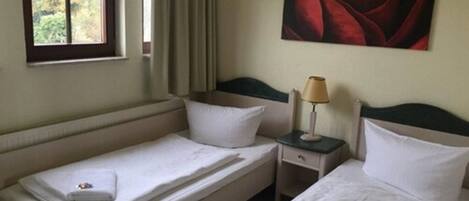 A hotel room with two single beds, a nightstand with a lamp, and a large window with curtains.