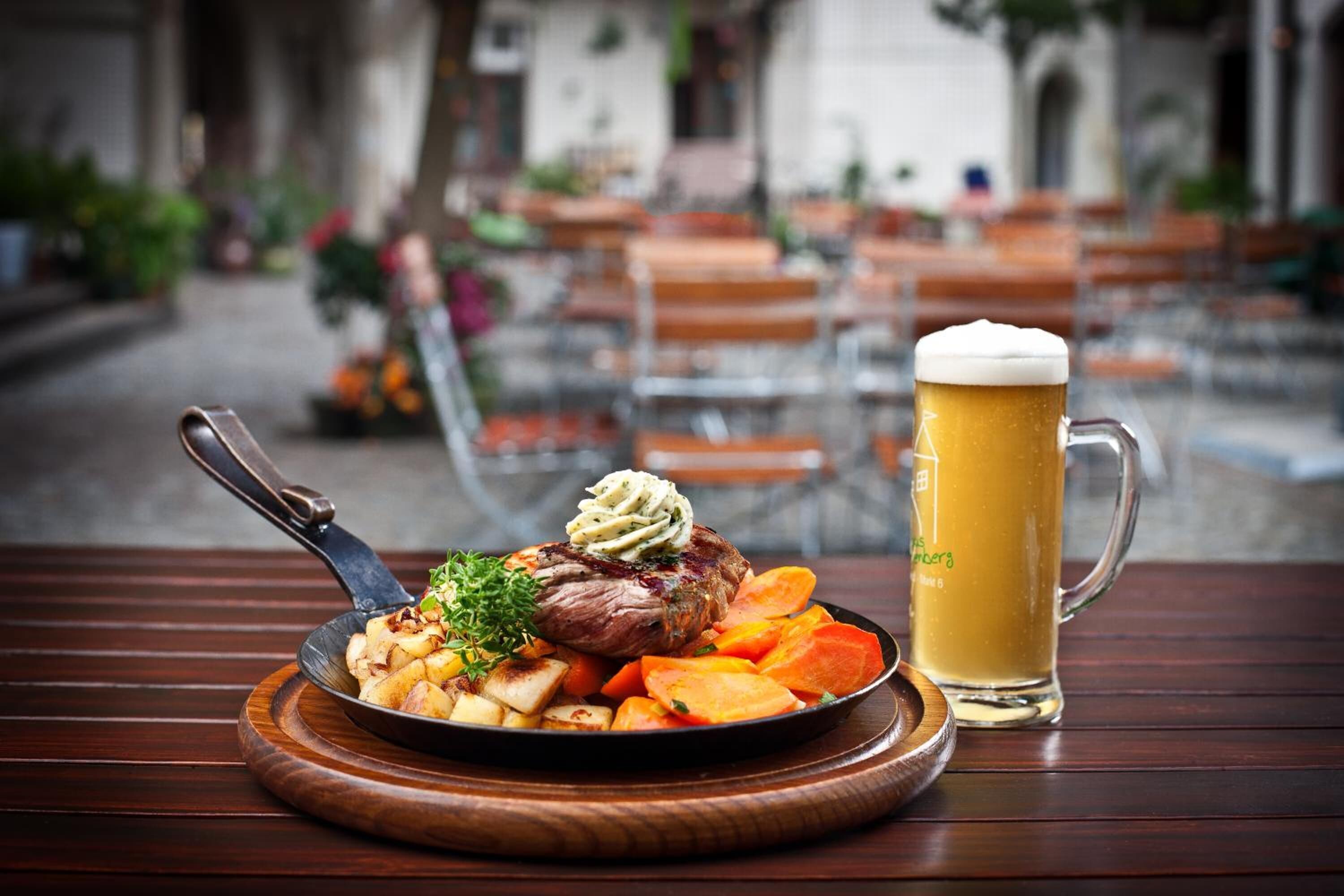 A meal with steak, roasted potatoes, and carrots, and a mug of beer on a wooden table.