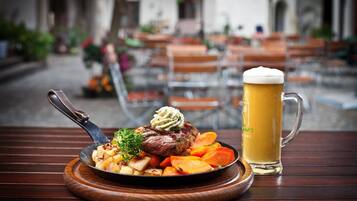 A meal with steak, roasted potatoes, and carrots, and a mug of beer on a wooden table.