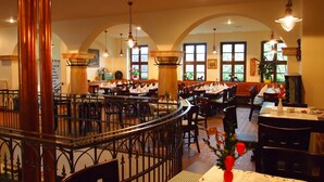 Een restaurant met meerdere eettafels en stoelen, hoge gewelfde plafonds en hangende lampen.