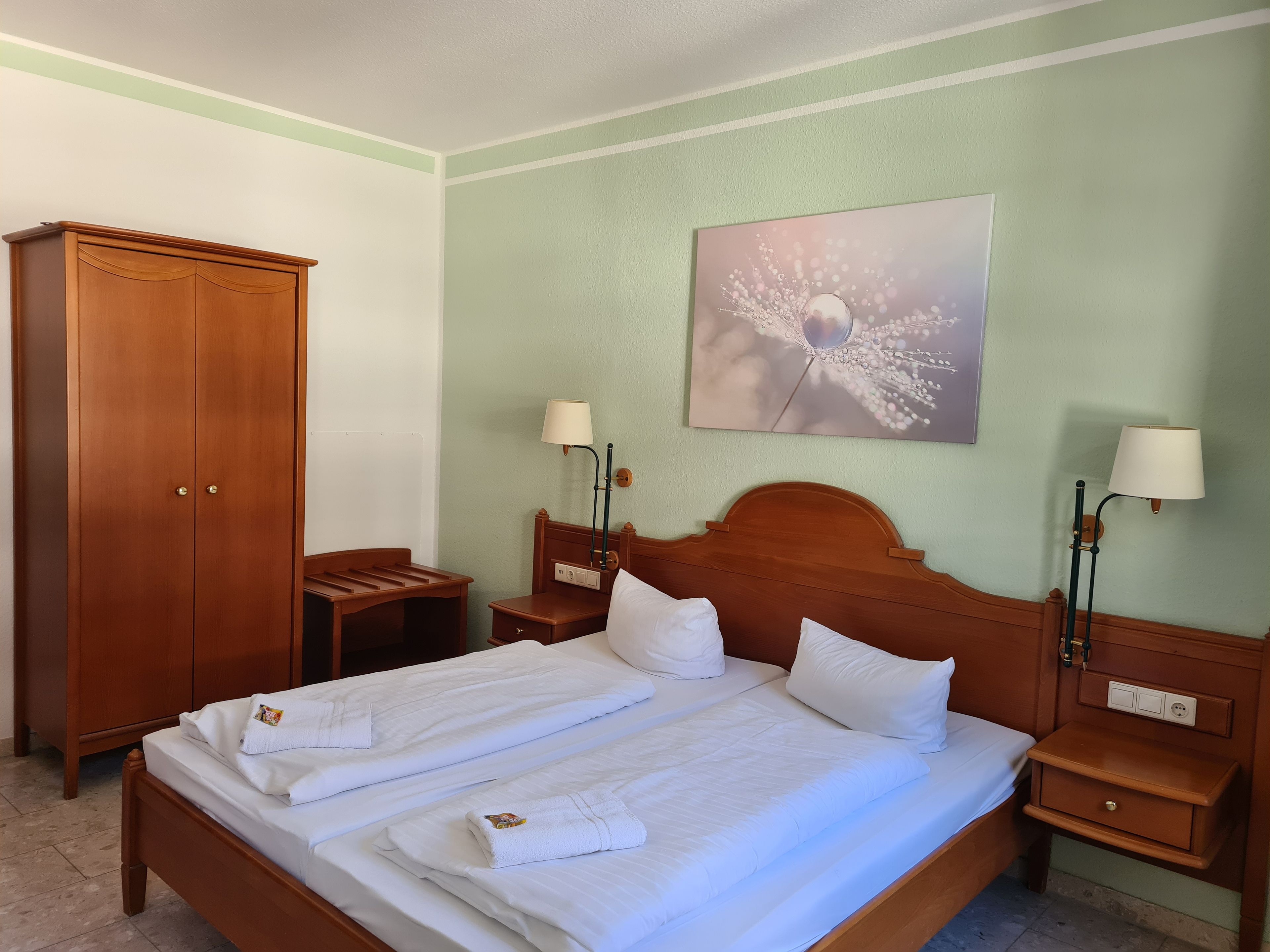 A hotel room with a double bed, two bedside tables with lamps, a wardrobe, and a wall-mounted artwork.
