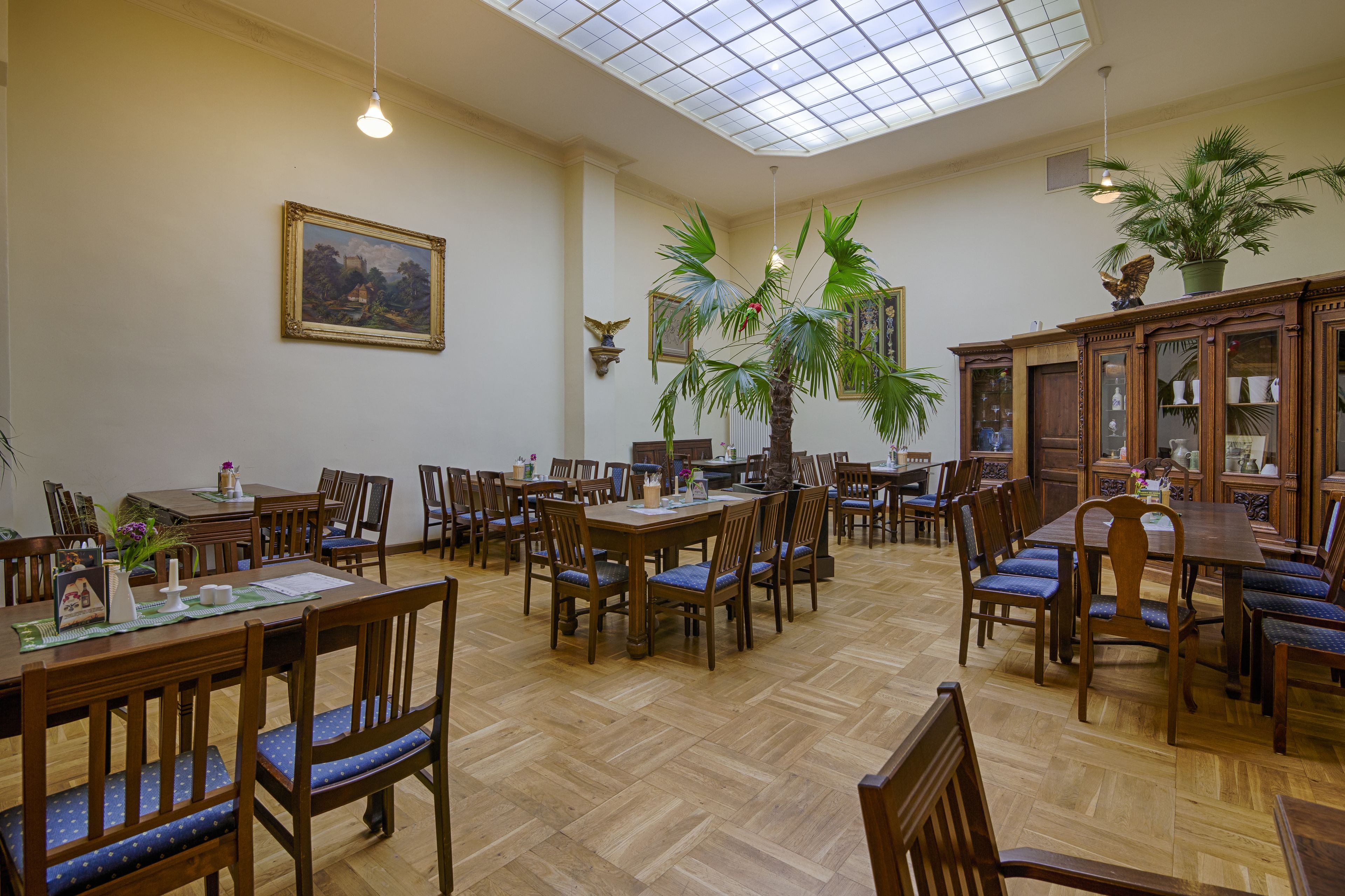 A dining area with wooden tables and chairs, a large potted plant, and a ceiling with a skylight.