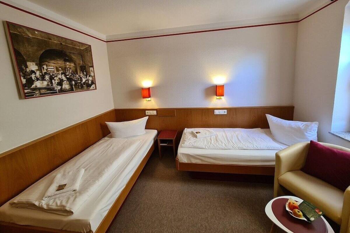 A hotel room with two single beds, a sofa, a small table with a fruit plate, and a painting on the wall.