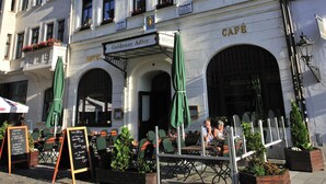 Een historisch gebouw met een café en restaurant op de begane grond, met terrasstoelen en groene parasols.