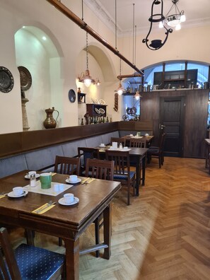 Un restaurant avec des tables et des chaises en bois, un parquet à motifs en chevrons et un lustre.