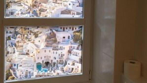 Un baño con dos ventanas que ofrecen vistas a un pueblo encalado con edificios y un molino.