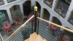 Un interior de varios niveles con una escalera central, varios balcones con plantas en macetas y diversas opciones de estar.