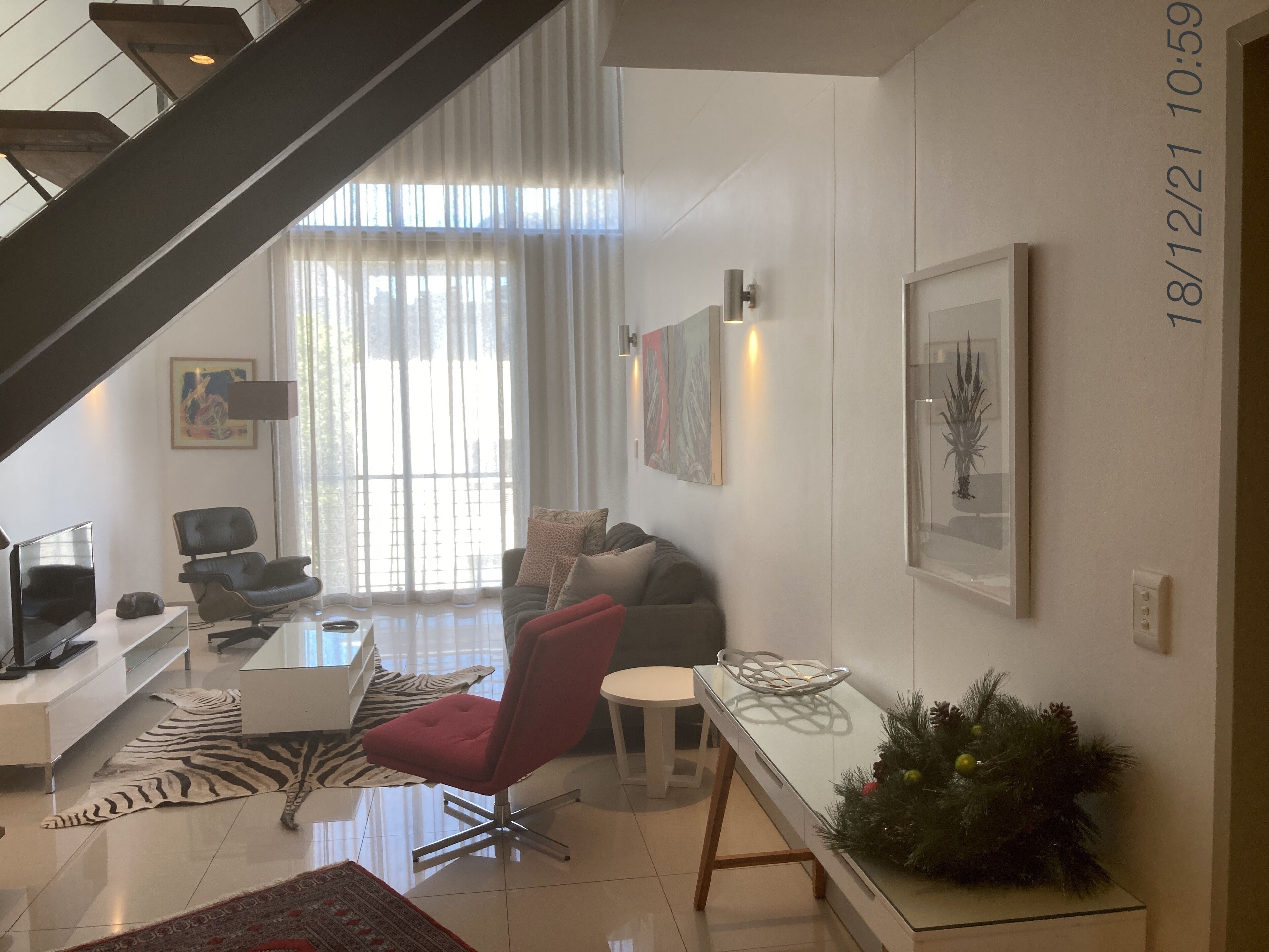 A modern living room with a staircase, a sofa, a red chair, a coffee table, and a TV.