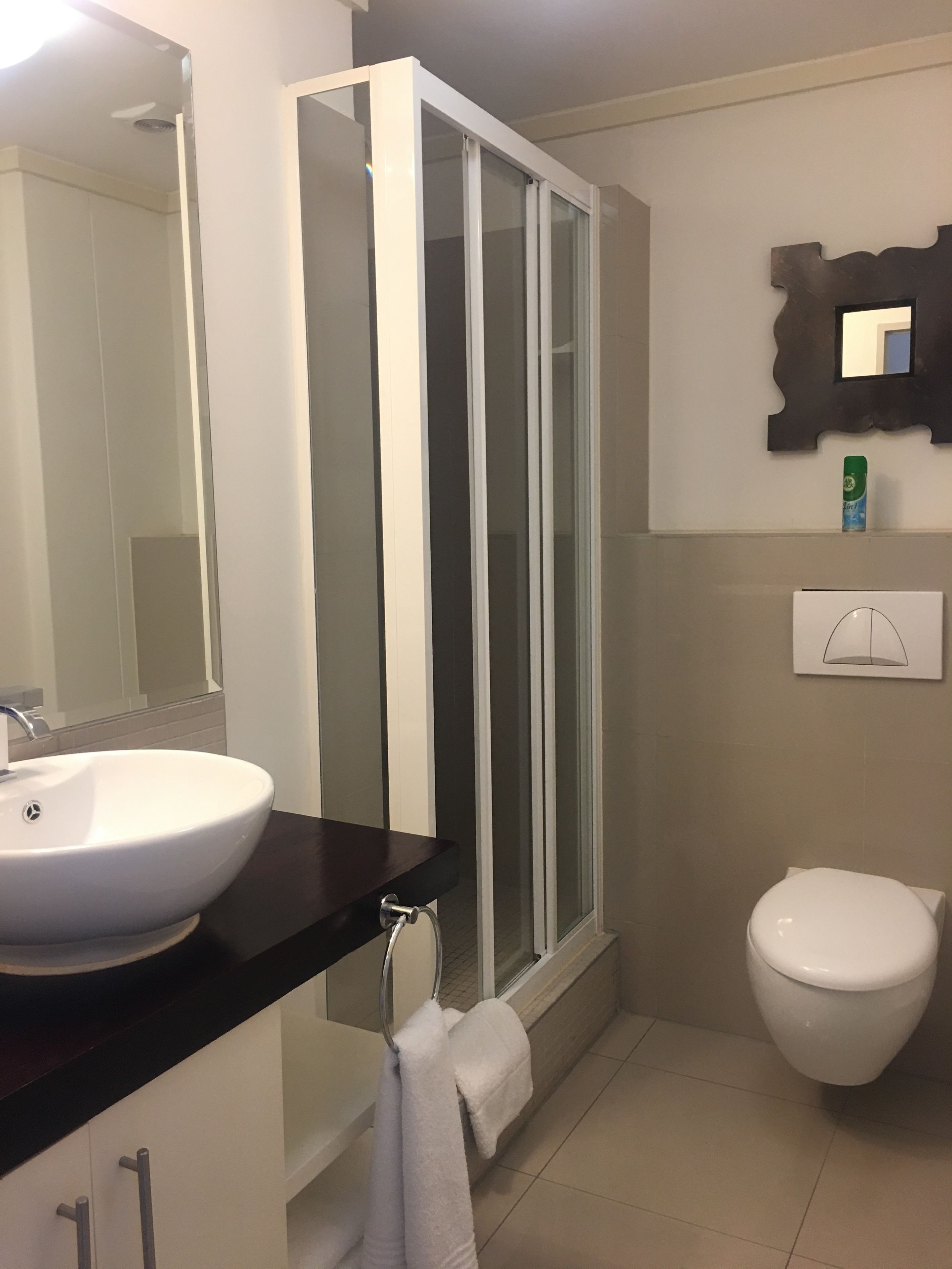 A modern bathroom with a white sink, a glass shower enclosure, and a toilet.