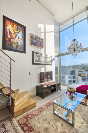 A modern living room with a staircase, a glass coffee table, and a large window with a city view. - The Quadrant Apartments (Cape Town)