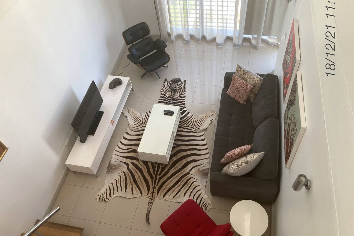 A modern living room with a zebra rug, a grey sofa with patterned cushions, a white side table, a red chair, and a black office chair.