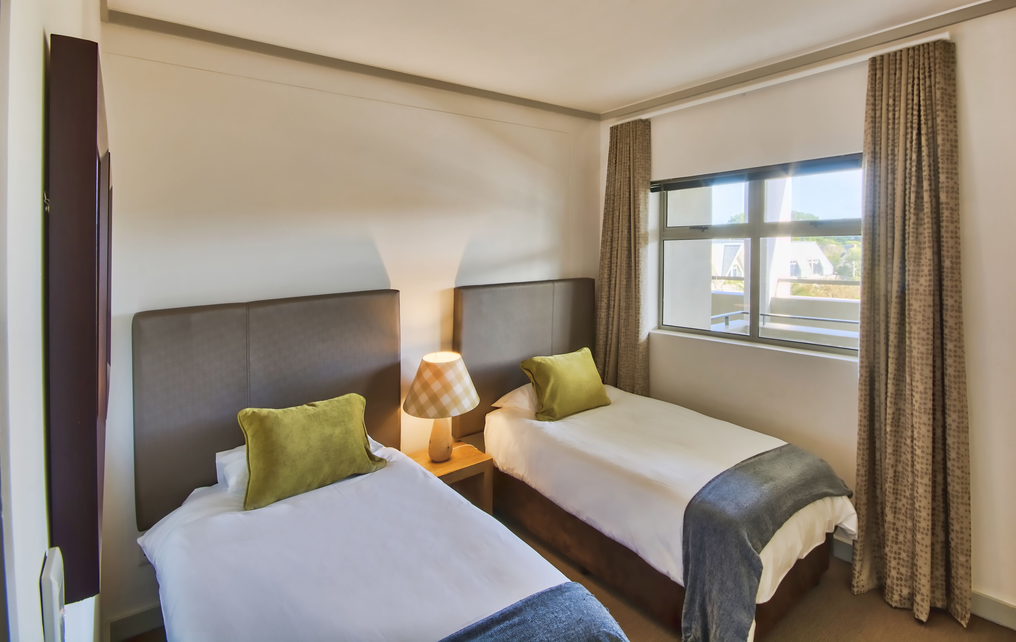 A hotel room with two beds, a nightstand with a lamp, and a window with curtains.