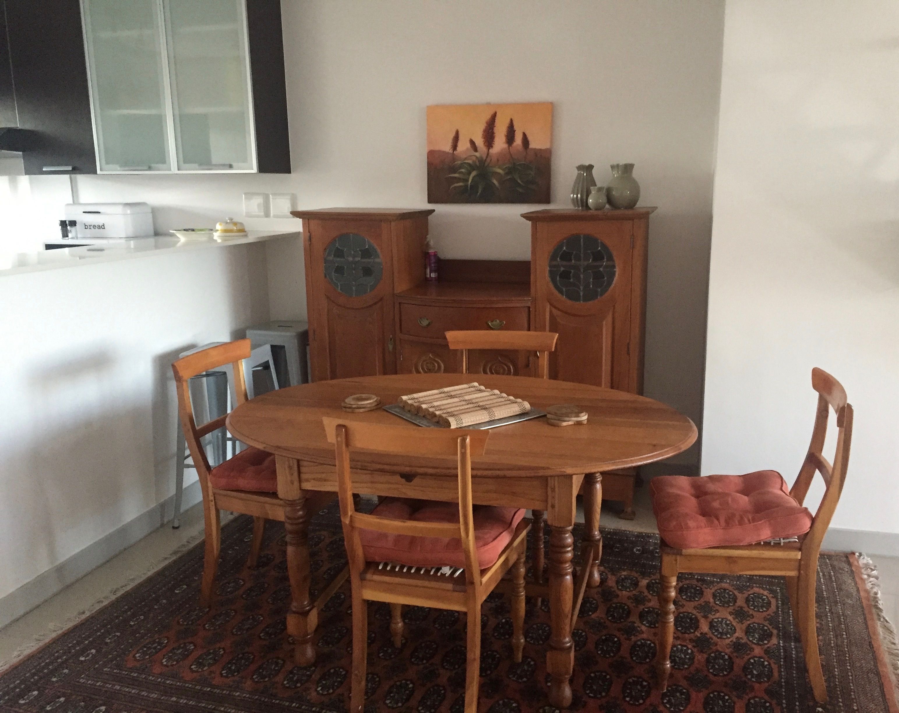 A dining area with a wooden table and chairs, a patterned rug, and a painting on the wall.